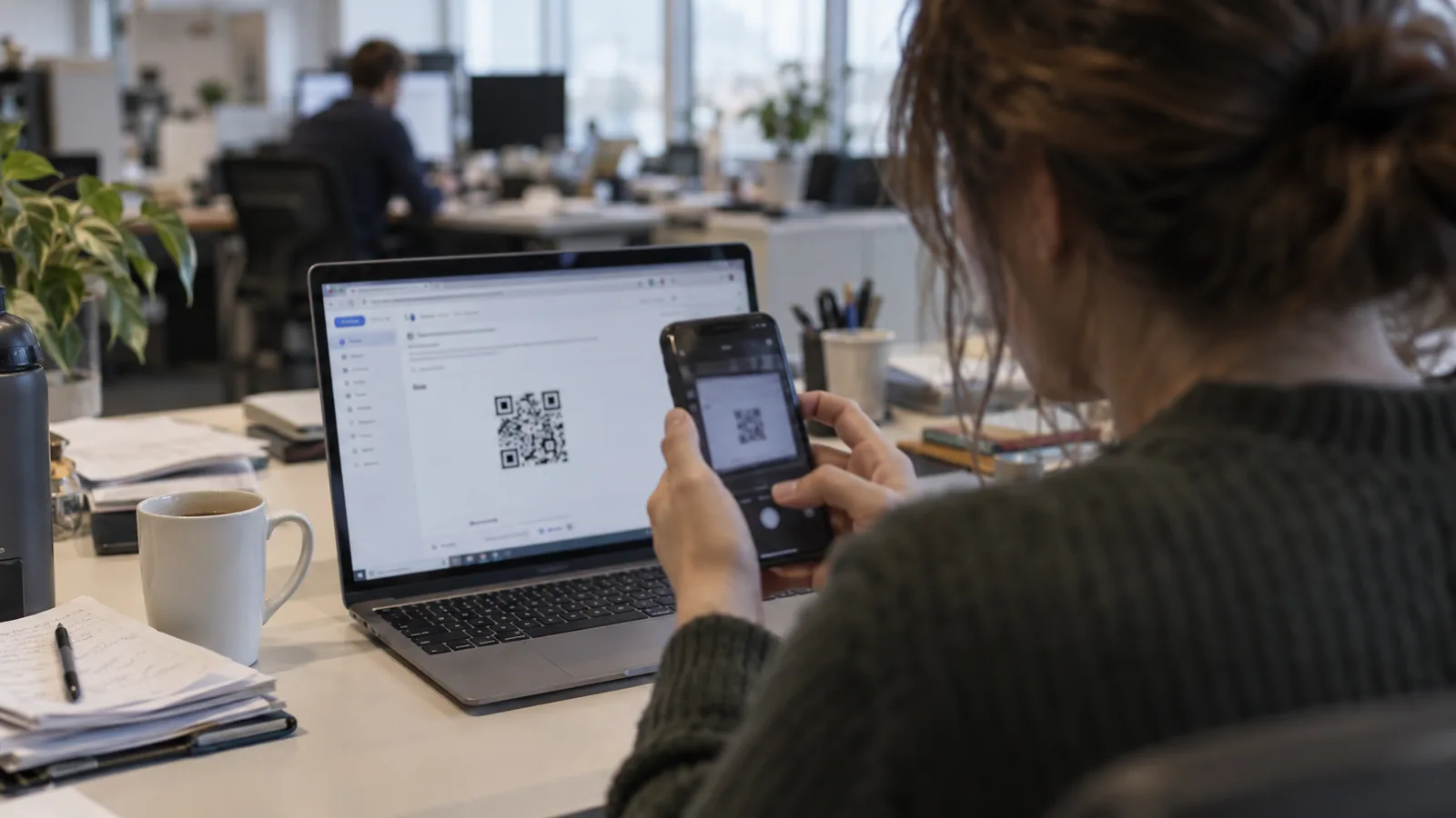 Pracownica skanuje smartfonem kod QR wyświetlony w wiadomości na ekranie laptopa.